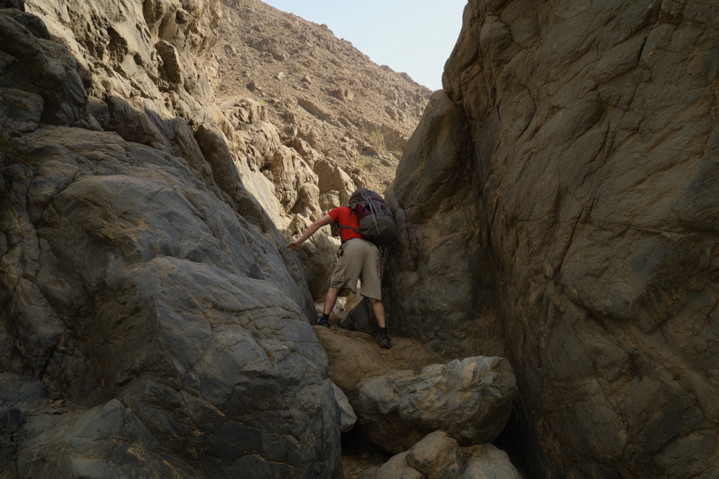 Hiker walking through narrow rocky section of Wadi Al Dhahir trail in Fujairah